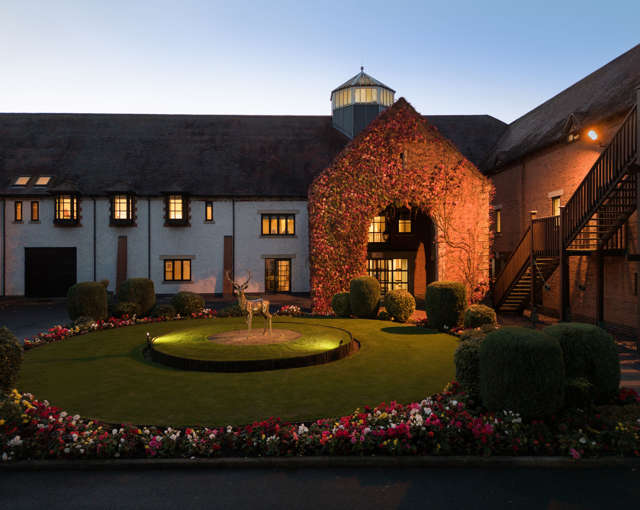 Evening exterior of Forest of Arden near Birmingham with ivy‑clad entrance, stag statue and circular flower garden